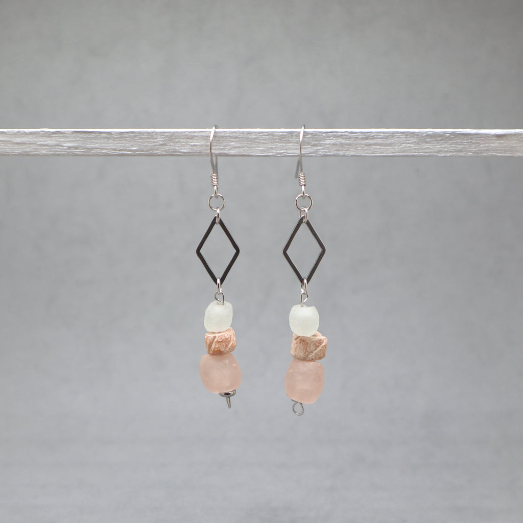Pair of earrings with diamond-shaped elements and pink and white beads on a gray background, recycled glass, bone and stainless steel silver