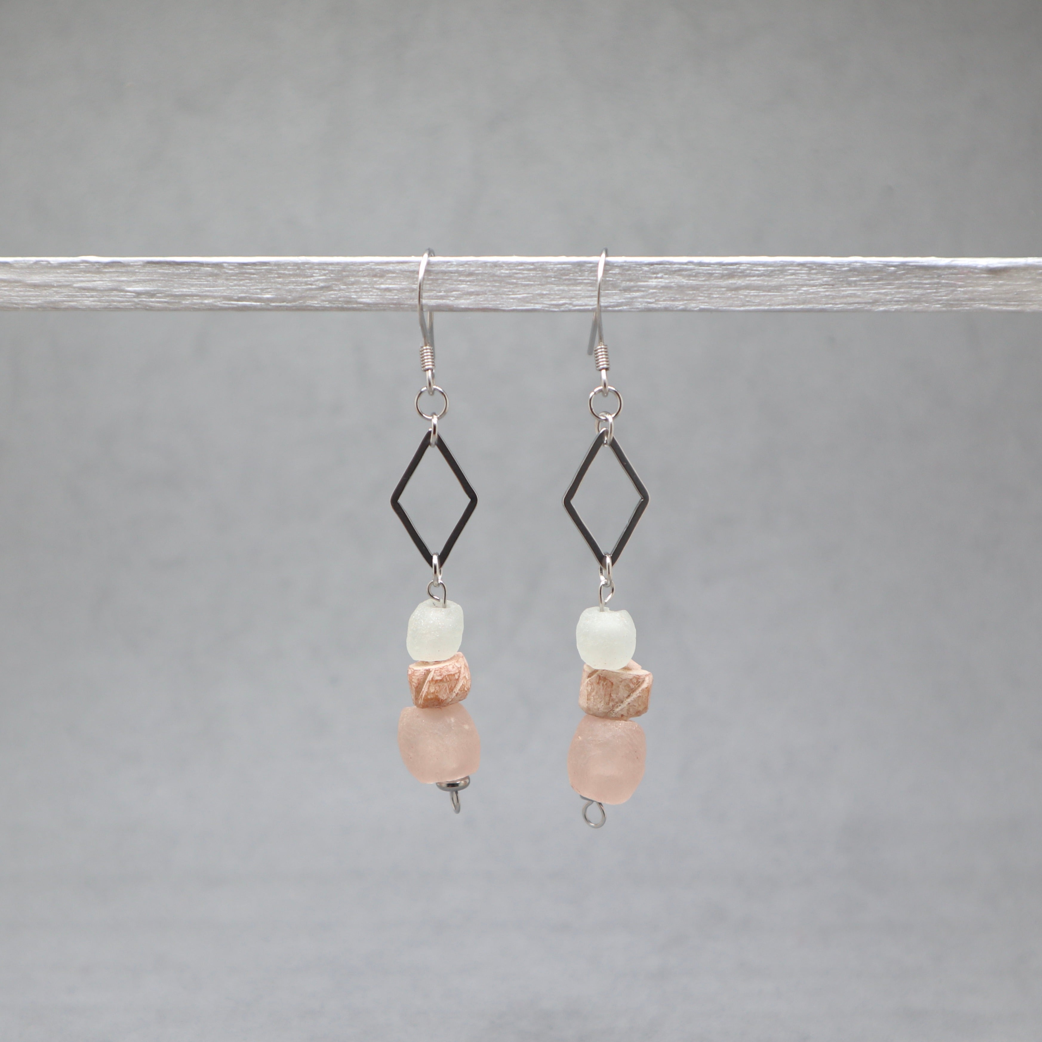 Pair of earrings with diamond-shaped elements and pink and white beads on a gray background, recycled glass, bone and stainless steel silver