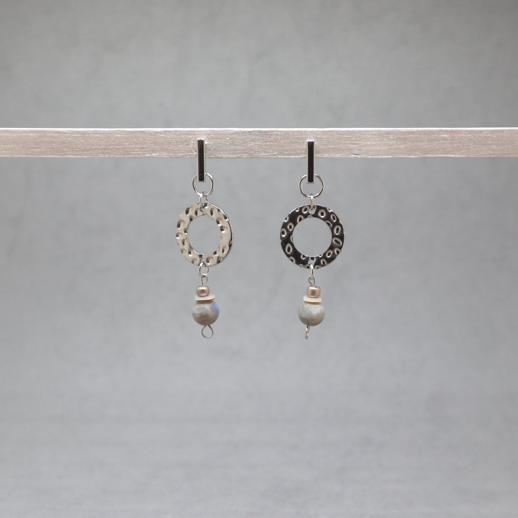 Pair of earrings with circular designs and beads hanging on a gray background, labradorite, stainless steel, heishi shell