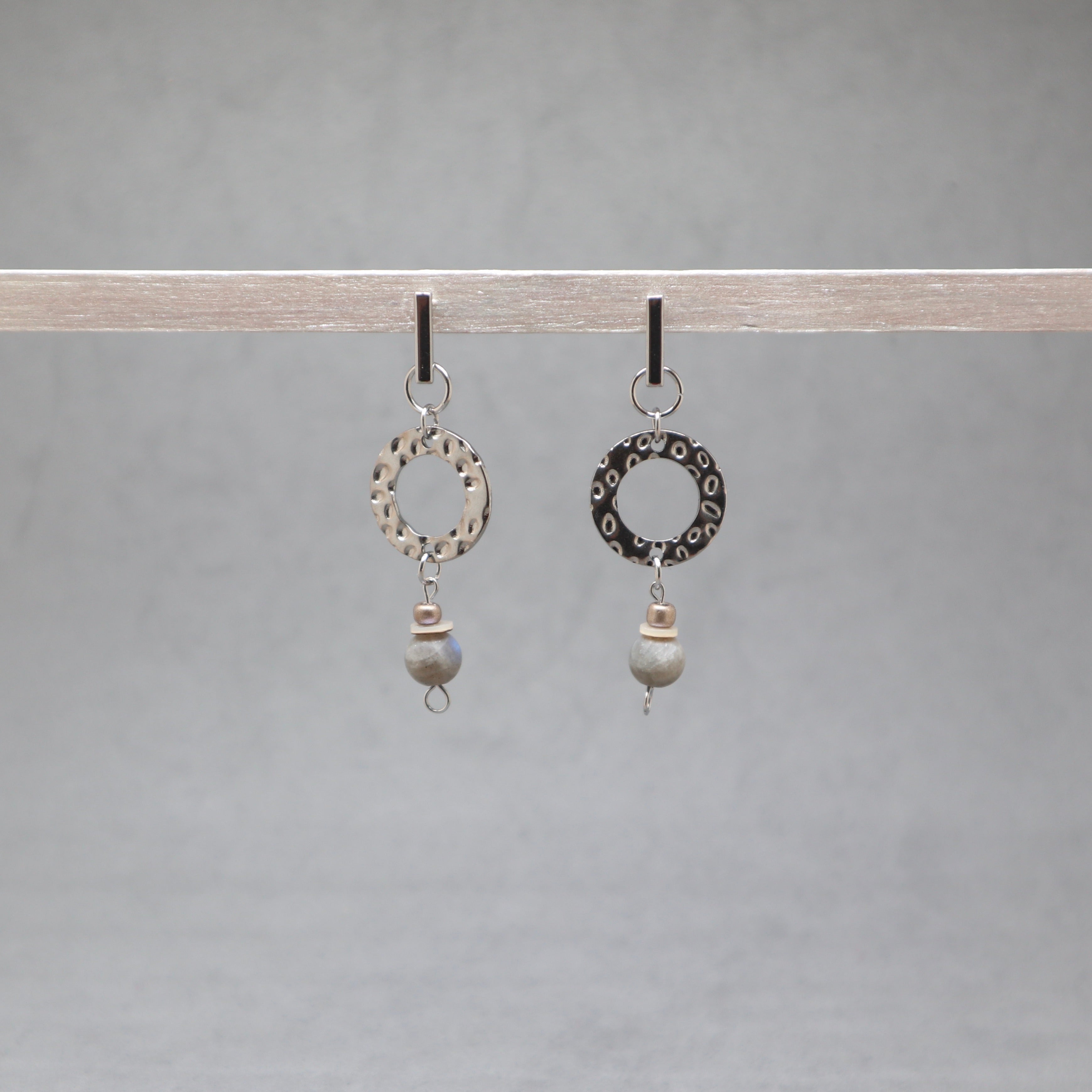 Pair of earrings with circular designs and beads hanging on a gray background, labradorite, stainless steel, heishi shell