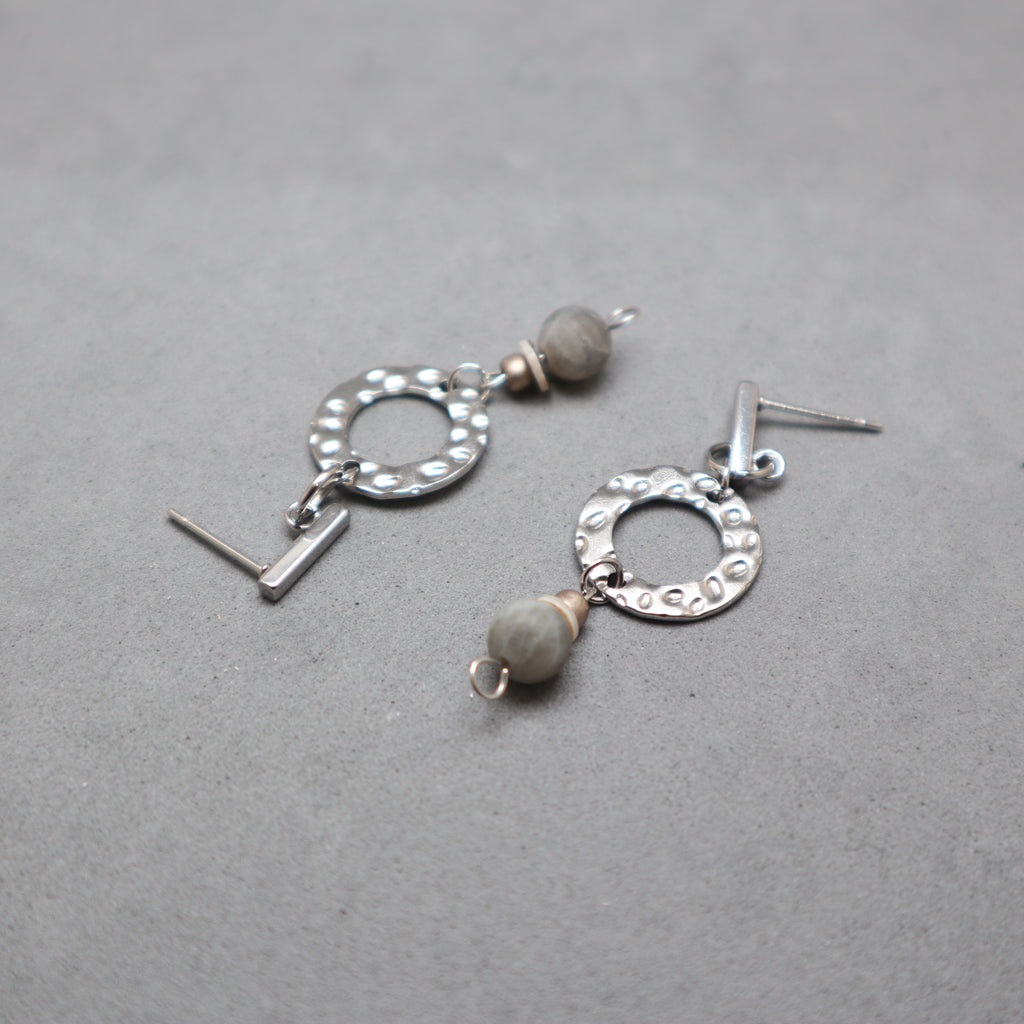 Silver earrings with circular designs and gray beads on a gray background