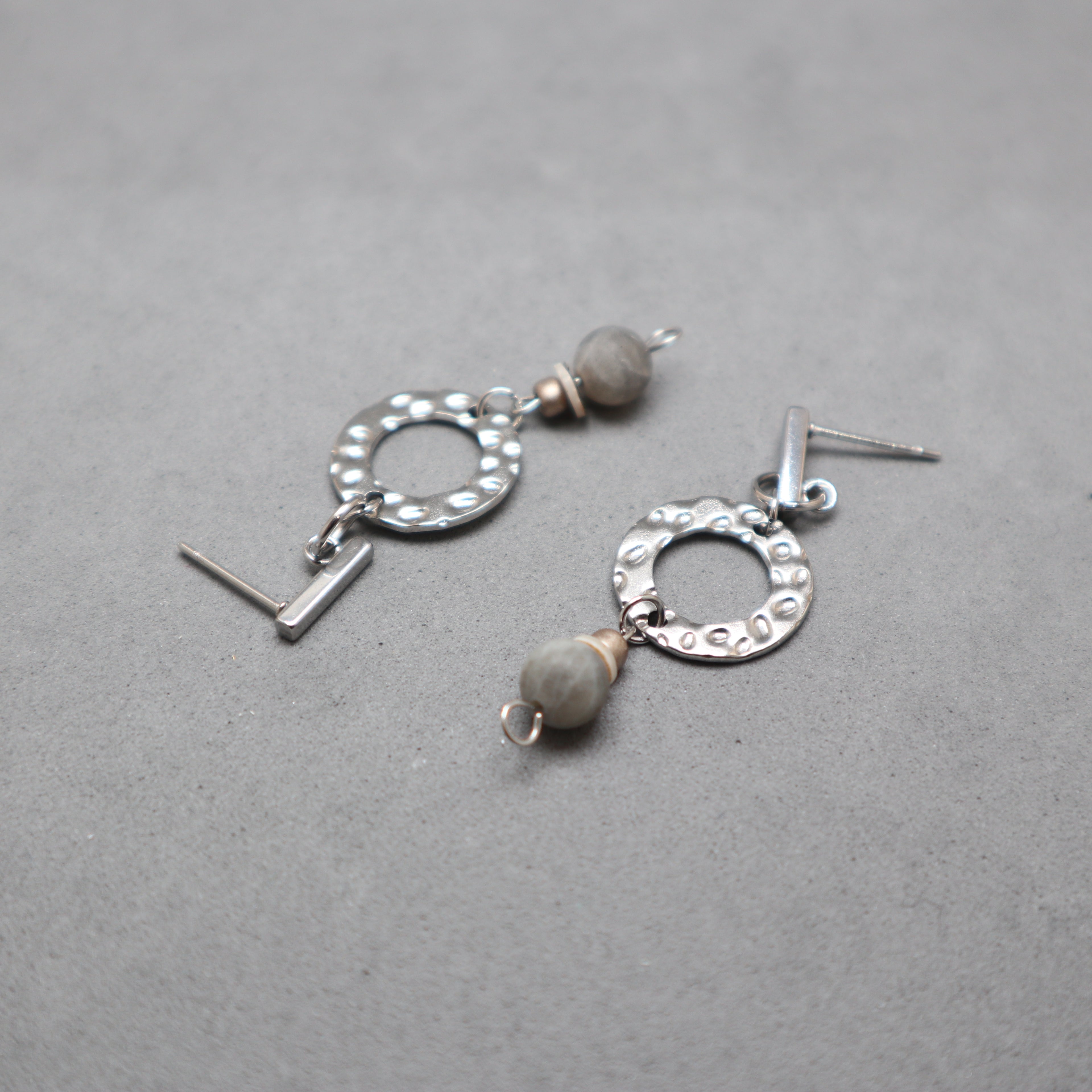 Silver earrings with circular designs and gray beads on a gray background