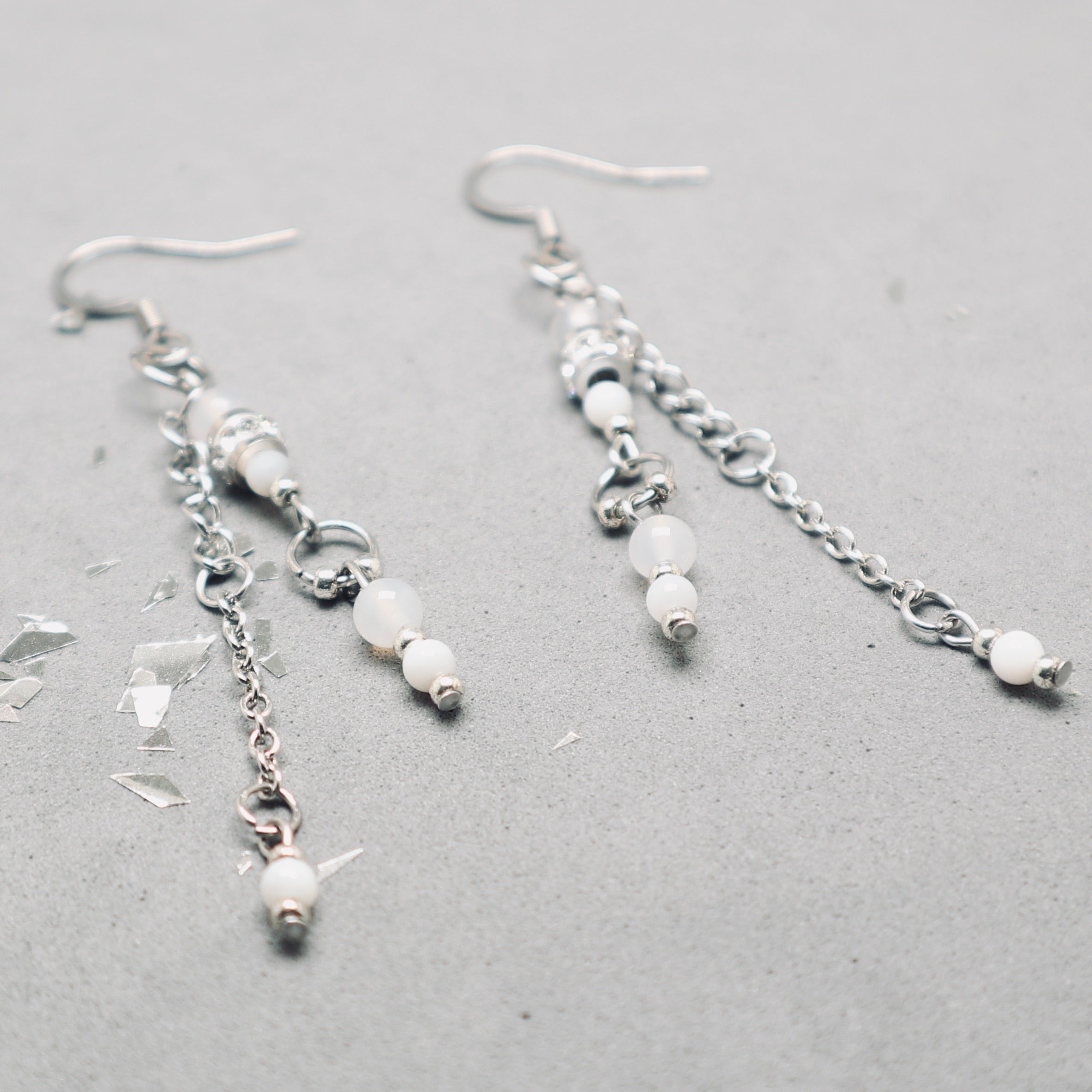 Silver earrings with beads on a gray surface