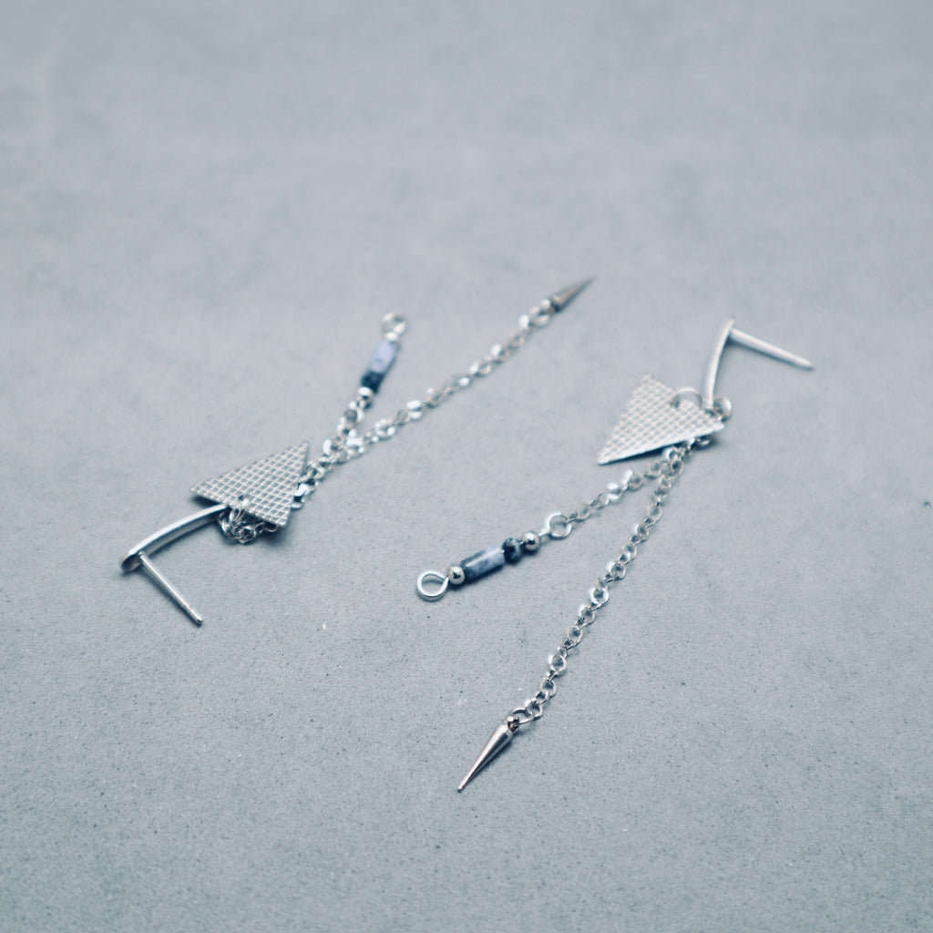 Silver earrings with chain and geometric design on a gray background