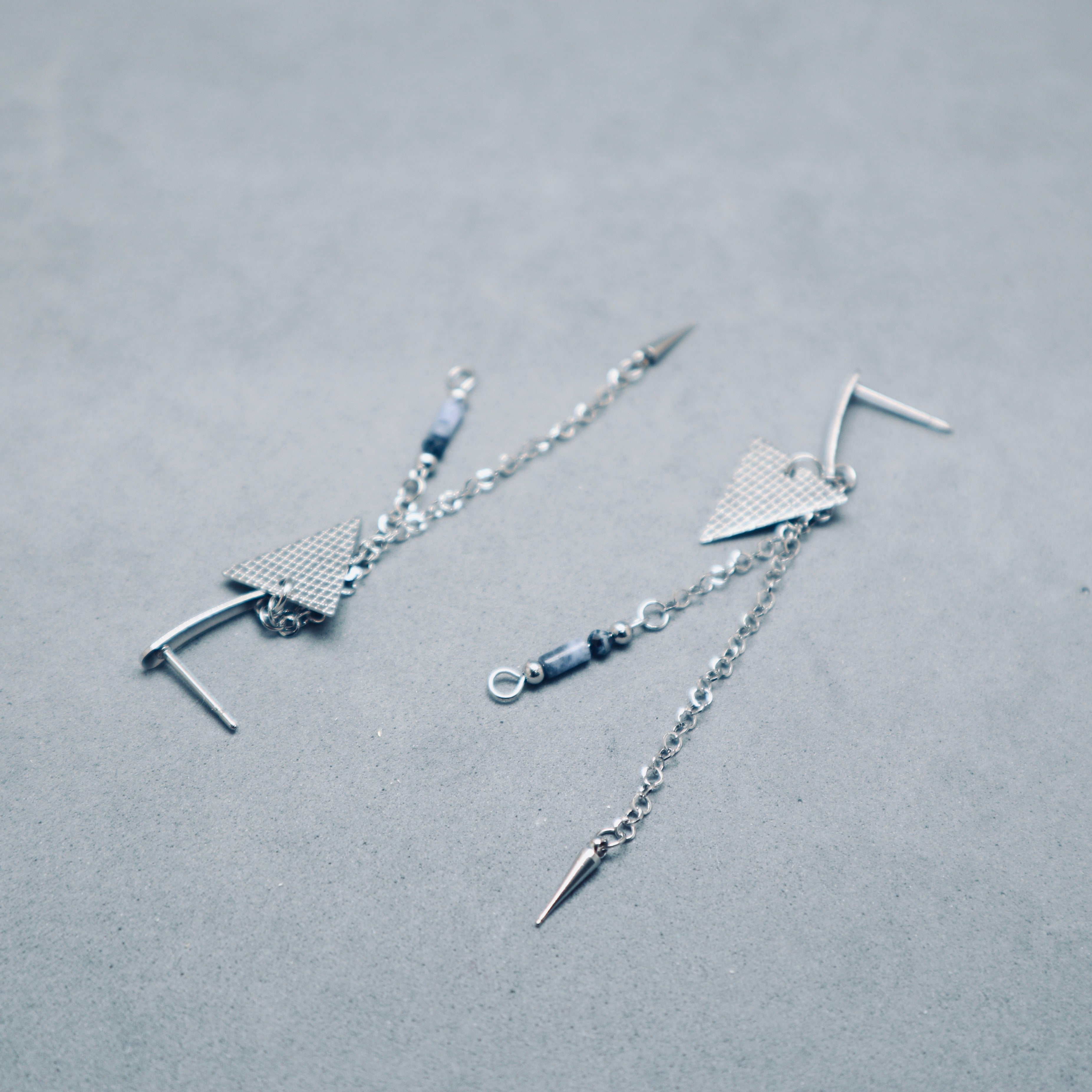 Silver earrings with chain and geometric design on a gray background