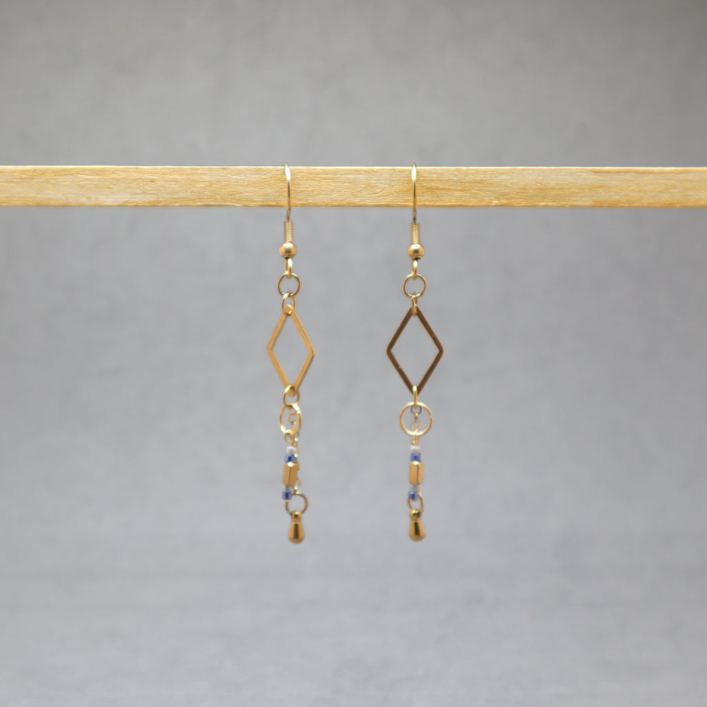 Gold earrings with diamond-shaped hooks and small beads on a gray background, stainless steel
