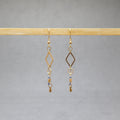 Gold earrings with diamond-shaped hooks and small beads on a gray background, stainless steel