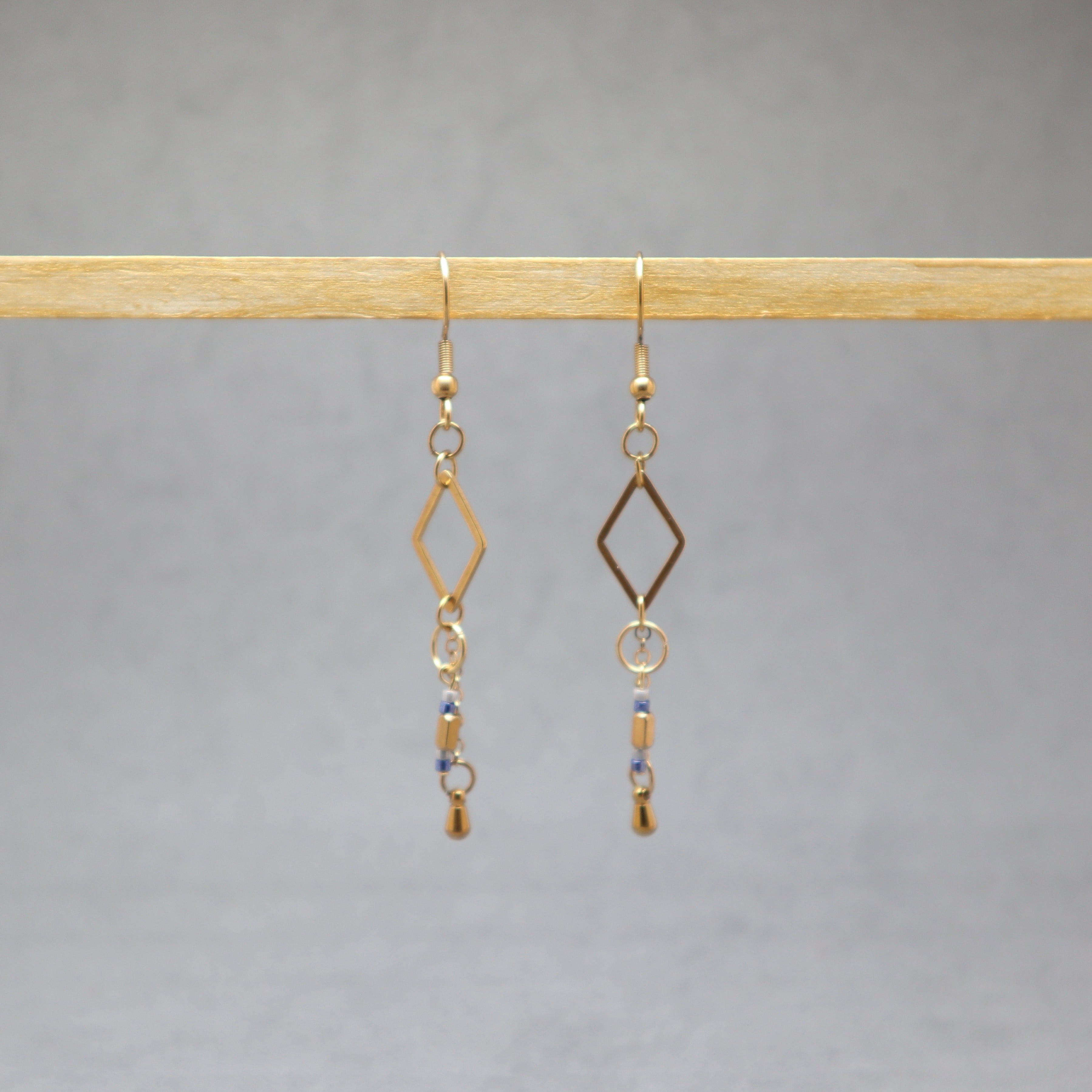 Gold earrings with diamond-shaped hooks and small beads on a gray background, stainless steel