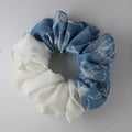 Two colors scrunchies, one white and one blue with a floral pattern, on a light gray background.