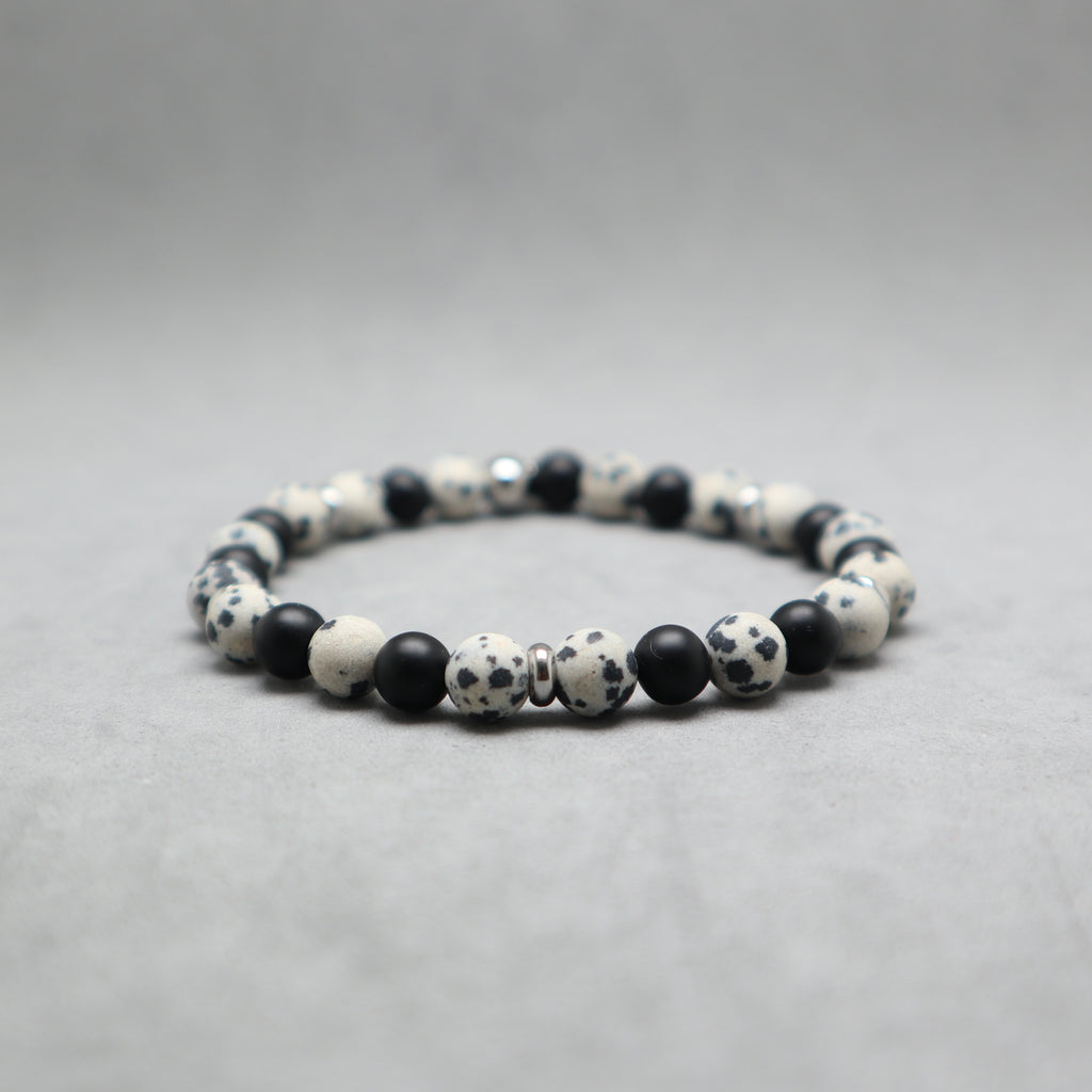 A beaded stretch bracelet made of black and white spotted round beads, with a few smooth black spacer beads, photographed on a neutral gray background.