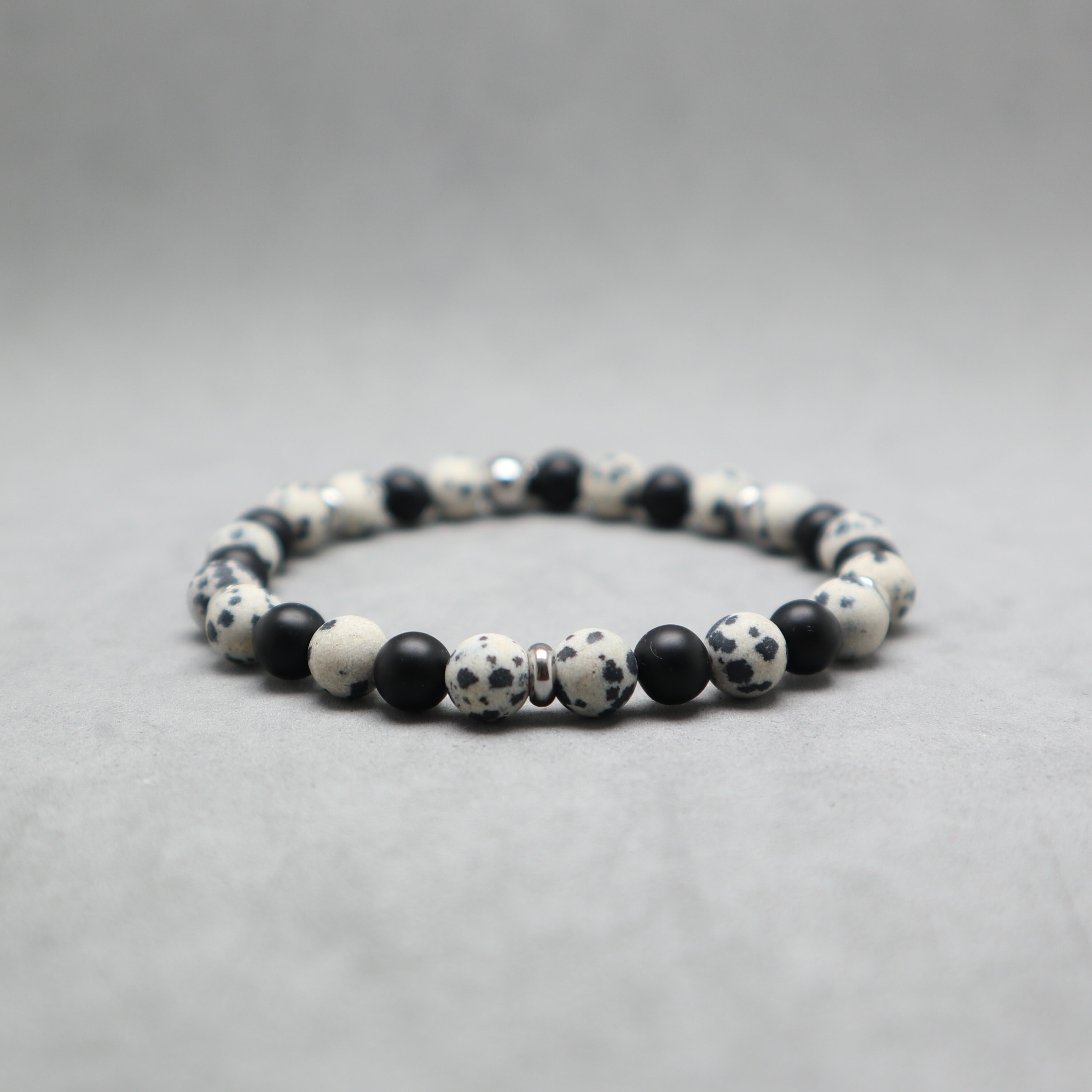 A beaded stretch bracelet made of black and white spotted round beads, with a few smooth black spacer beads, photographed on a neutral gray background.